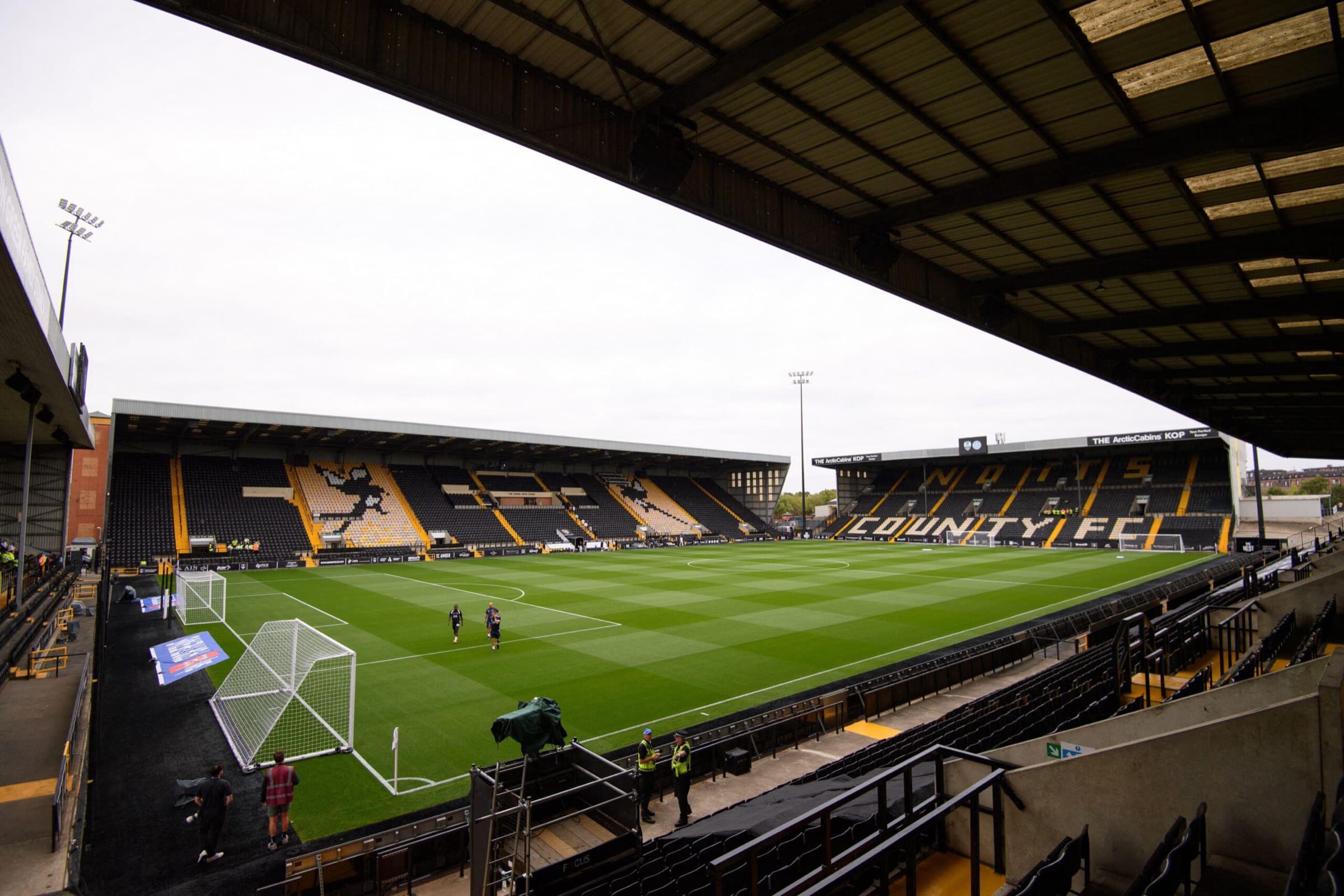 Inside a football ground before kick-off, seen from under the stand roof